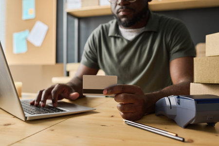 Close-up of African man sitting at table and using laptop to pay online with credit cardの写真素材