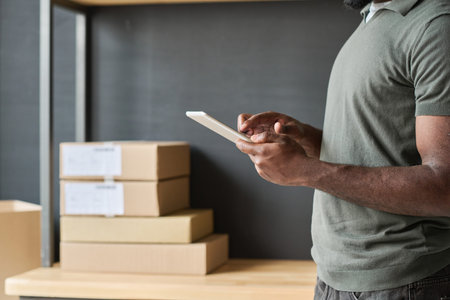 Close-up of African man typing on digital tablet doing online work in warehouseの写真素材