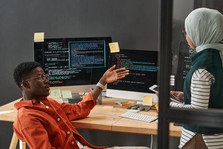 Young confident African American man making presentation of decoded data to female colleague in...