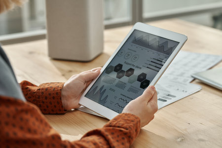 Close-up of businesswoman examining graphs on the screen of tablet pc while sitting at table at officeの写真素材