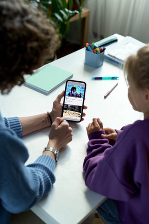 High angle view of mother and her child watching video together on smartphone while having activity at deskの写真素材