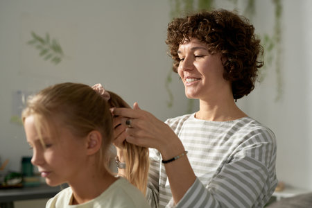 Young smiling mother making hairstyle to her child, she getting her ready for school