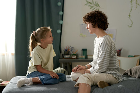 Mother having openly conversation with her daughter while they sitting on bed in bedroomの写真素材
