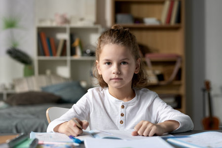 Portrait of little boy sitting at desk with books and looking at camera, he studying at homeの写真素材