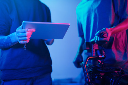 Director using digital tablet and discussing project with camera operator before shootingの写真素材