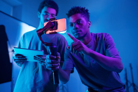 African American operator using special technique to shoot video on smartphone with his colleague...