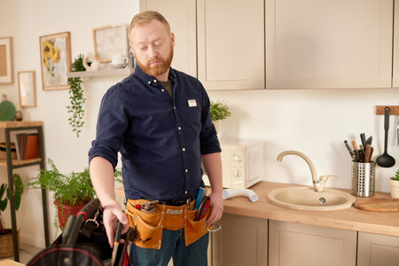 Repairman using work tools to fix sink and faucet during his work in domestic kitchenの写真素材
