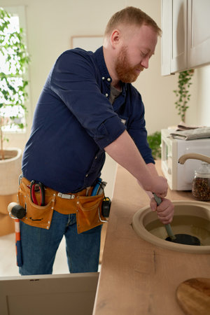 Mature worker repairing blockage in the sink with special equipment during his work in domestic kitchenの写真素材
