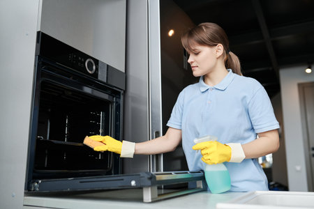 Young woman cleaning the oven with detergent in the kitchen during professional houseworkの写真素材