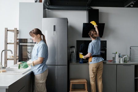 Professional cleaning workers wiping dust from furniture while doing housework in team in the kitchenの写真素材