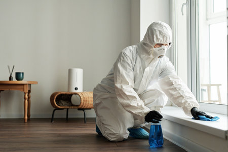 Cleaning worker in protective suit disinfecting surface with detergent during housework at homeの写真素材