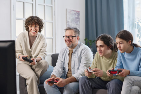 Happy family of four playing game console together while sitting on sofa in the room at homeの写真素材