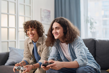 Teenage boy playing game console together with his mom during their leisure time at homeの写真素材