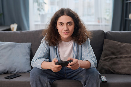 Portrait of teenage boy looking at camera while sitting on sofa with joystick, he playing video gameの写真素材