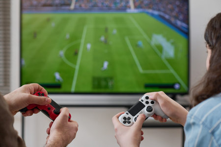 Rear view of boy playing video game together with his mom while they sitting in front of TV screen