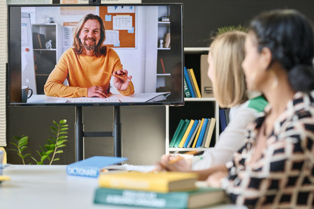 Group of students sitting in front of screen and talking to teacher online during video call in classの写真素材