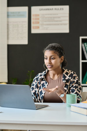 Vertical image of student sitting at desk in front of laptop and talking to teacher online on laptopの写真素材