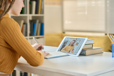 Close-up of girl making notes while talking to teacher during video call on tablet pcの写真素材