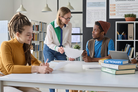 Young teacher explaining material to student pointing at paper while they studying foreign language...