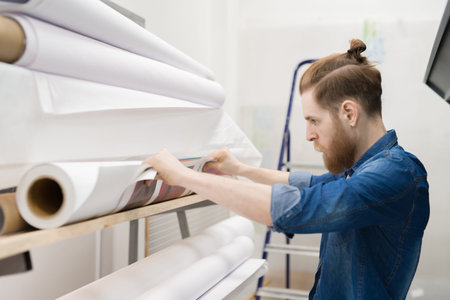 Concentrated handsome young man viewing printing roll of paper for printing order in office