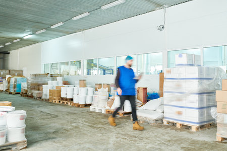 Blurred motion of busy warehouse manager in uniform reading online records on tablet while hurrying to shipment stationの写真素材