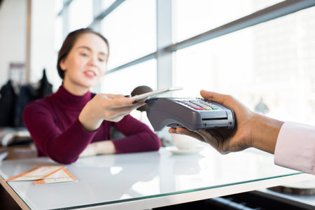 Close-up of beautiful businesswoman using smarphone to pay for restaurant bill and touching it with wireless credit card readerの写真素材
