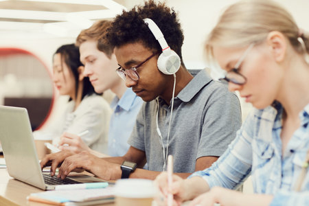 Serious busy Black student guy in glasses sitting at table with groupmatesの写真素材