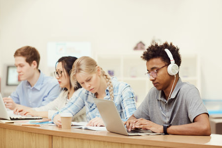 Group of serious young multi-ethnic students in casual clothing sitting at one table and preparing for seminar in lecture roomの写真素材