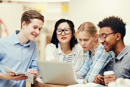 Confident Asian girl in glasses standing at table and pointing at laptop screen while showing presentation to group matesの写真素材