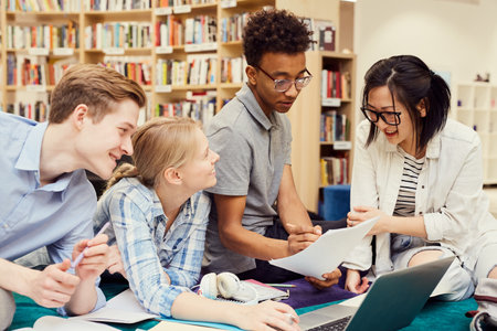 Group of positive young multi-ethnic students studiying in modern libraryの写真素材