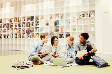 Group of pensive young interracial students sitting among papers and devices on floor in library and discussing ideas for joint projectの写真素材