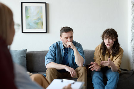 Young woman talking about her family problems to psychologist while they sitting on sofa together with her husbandの写真素材
