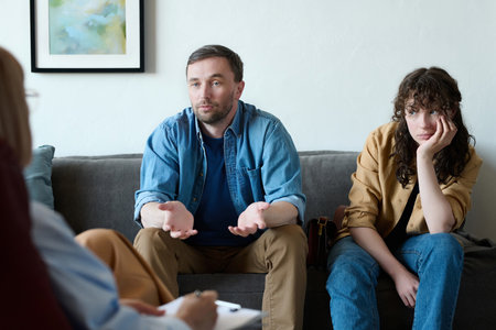 Young man talking to psychologist about problems with his wife during session in officeの写真素材