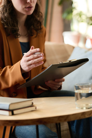 Vertical image of young therapist with folder of document talking during sessionの写真素材