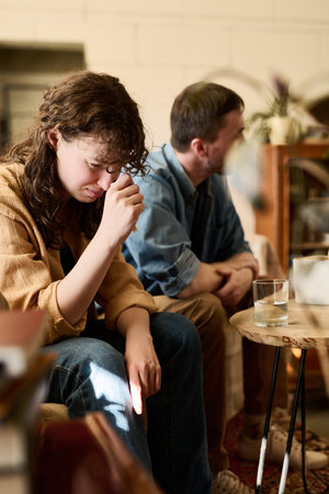 Vertical image of stressed woman sitting on sofa and crying while visiting psychologist with husbandの写真素材