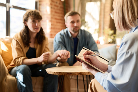 Therapist examining problems of couple making notes in her notepad during conversation with couple at sessionの写真素材