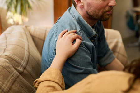 Close-up of mature man sitting on sofa in depression supporting by woman during psychotherapyの写真素材