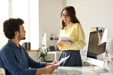 Young businesswoman with tablet pc discussing online work with her colleague in officeの写真素材