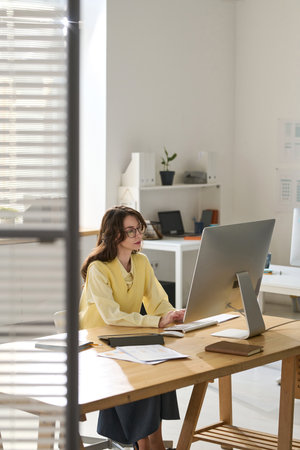 Vertical image of young businesswoman working on computer in modern officeの写真素材