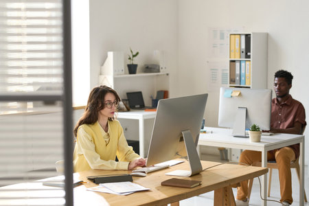 Young business people sitting at their workplaces and working on computers in modern officeの写真素材
