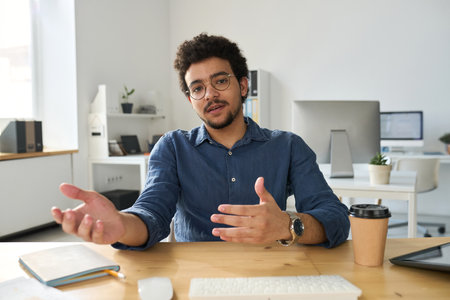 Young businessman sitting at his workplace and discussing working moments during video call on computerの写真素材