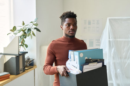 African American businessman carrying box with office stuffs during the move in new officeの写真素材