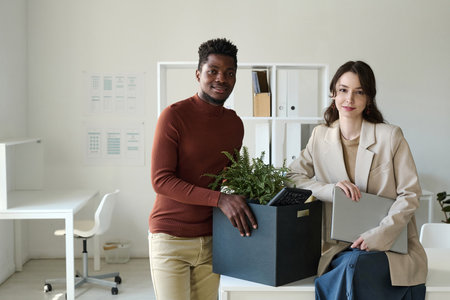 Portrait of young couple of colleagues smiling at camera while moving to new officeの写真素材