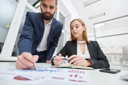Concentrated young accountants examining financial report together and discussing growth prospects at meeting in modern officeの写真素材