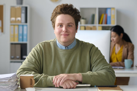 Portrait of young businessman sitting at his workplace in office and looking at cameraの写真素材