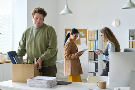 Upset businessman packing his things in box during leaving his workplace in office after layoffの写真素材
