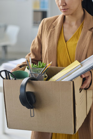 Vertical image of businesswoman packing things in box after job lossの写真素材