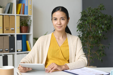 Portrait of young pregnant businesswoman looking at camera while sitting at her workplace and working on tablet pcの写真素材