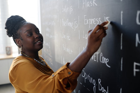 African American teacher standing near the blackboard and teaching IT material at lessonの写真素材