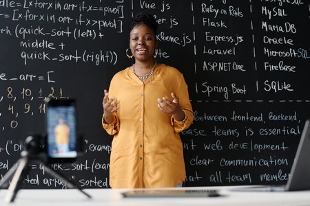 Young African American teacher talking about IT in her blog standing against blackboard at classの写真素材